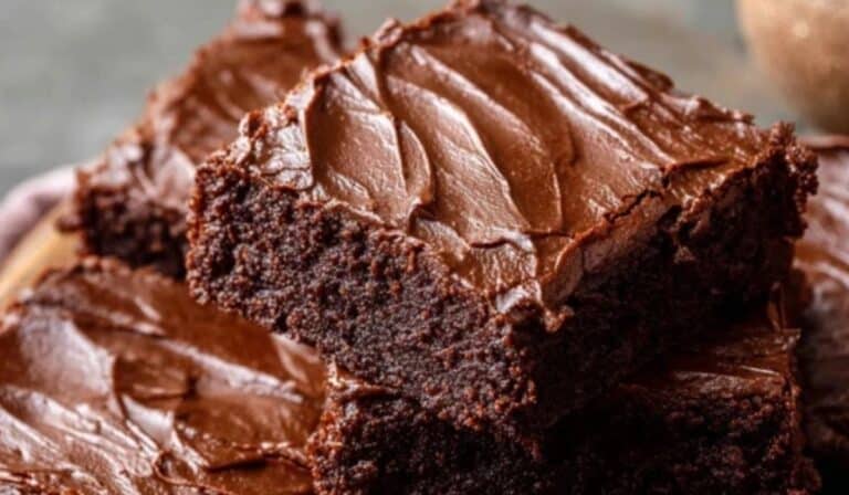 Chewy fudgy frosted brownies stacked on a wooden table with rich chocolate frosting