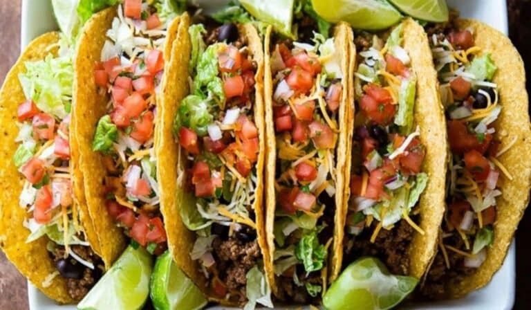 Ground Beef Tacos with pico, cheese, lettuce, and lime on a wooden table